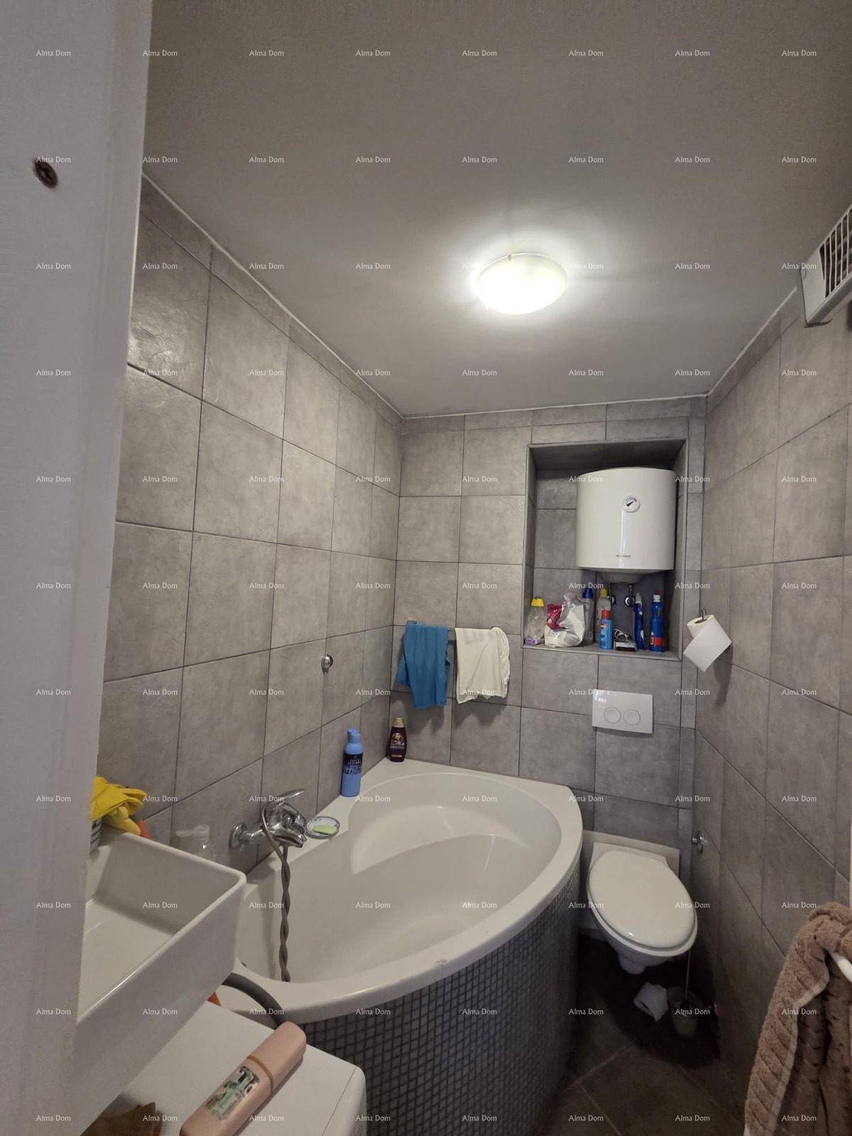Badezimmer mit grauen Fliesen, einer Eckbadewanne, Toilette und einem Waschbecken.