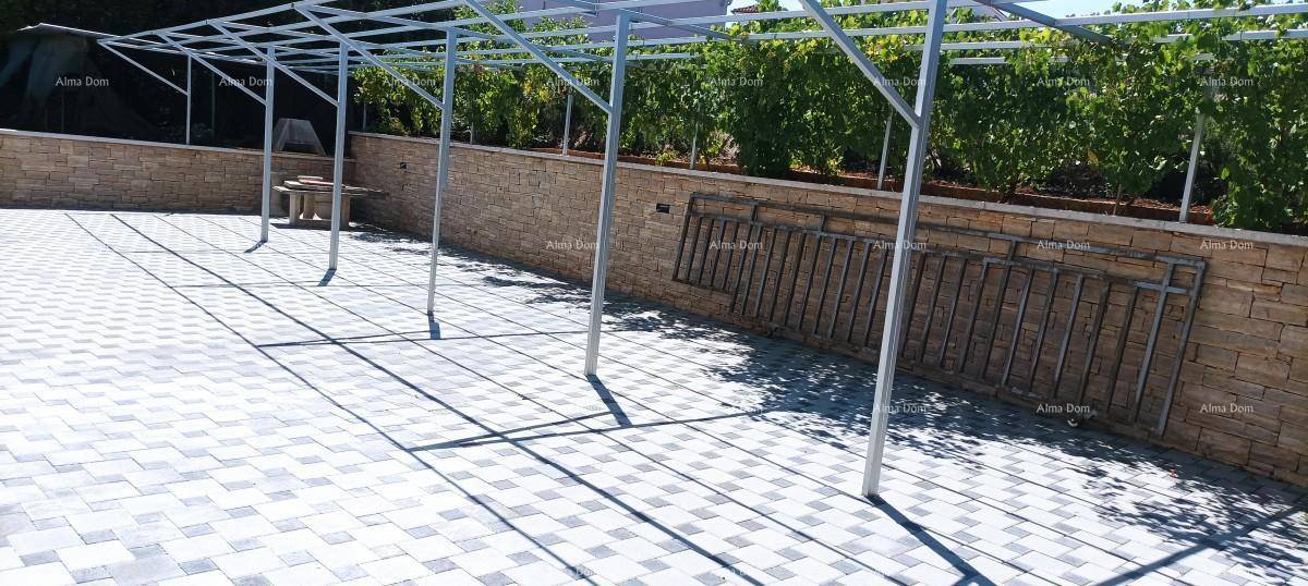 Gepflasterter Außenbereich mit einer Metallkonstruktion für eine zukünftige Überdachung und grüner Hecke.