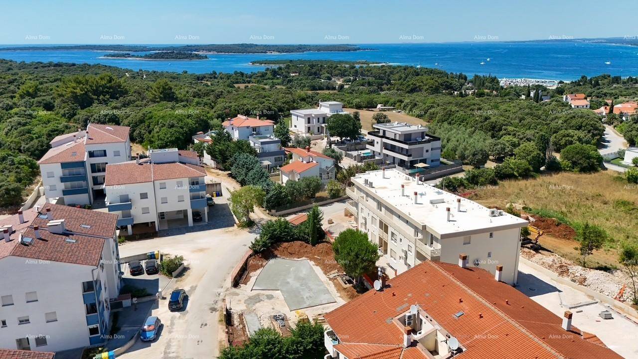 Luftaufnahme einer Küstensiedlung mit Wohngebäuden, viel Grün und dem Meer im Hintergrund unter blauem Himmel.