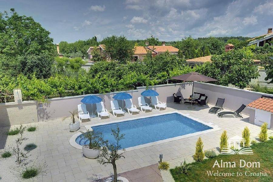 Überblick über den weitläufigen Gartenbereich mit Pool, Liegewiese und schattigen Sitzgelegenheiten.