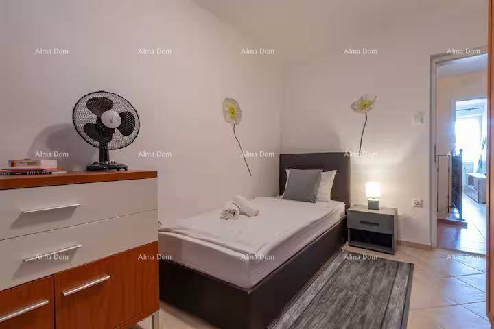 Schlafzimmer mit Einzelbett, Nachttisch, Ventilator und Blick in den Flur.