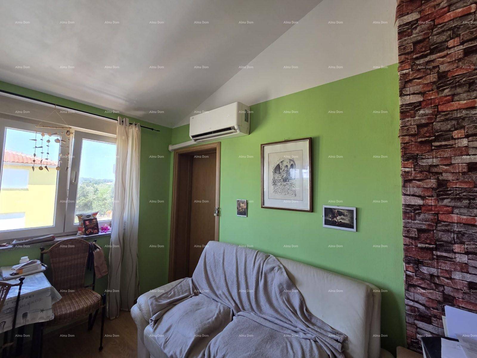 Heller Wohnbereich mit beigem Sofa, grünen Wänden, Ziegelwandakzent und Klimaanlage.