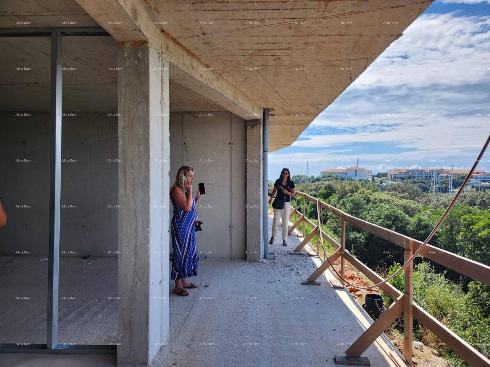 Zwei Personen auf einem Rohbau-Balkon betrachten den weiten Blick auf den Yachthafen und die Natur.