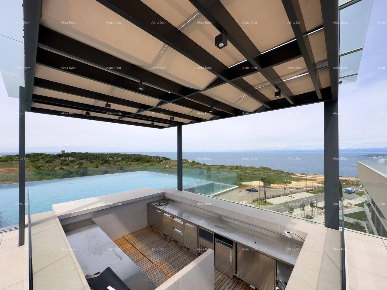Gut ausgestattete Außenküche unter einer schattenspendenden Pergola, mit Blick auf den Infinity-Pool und das Meer.