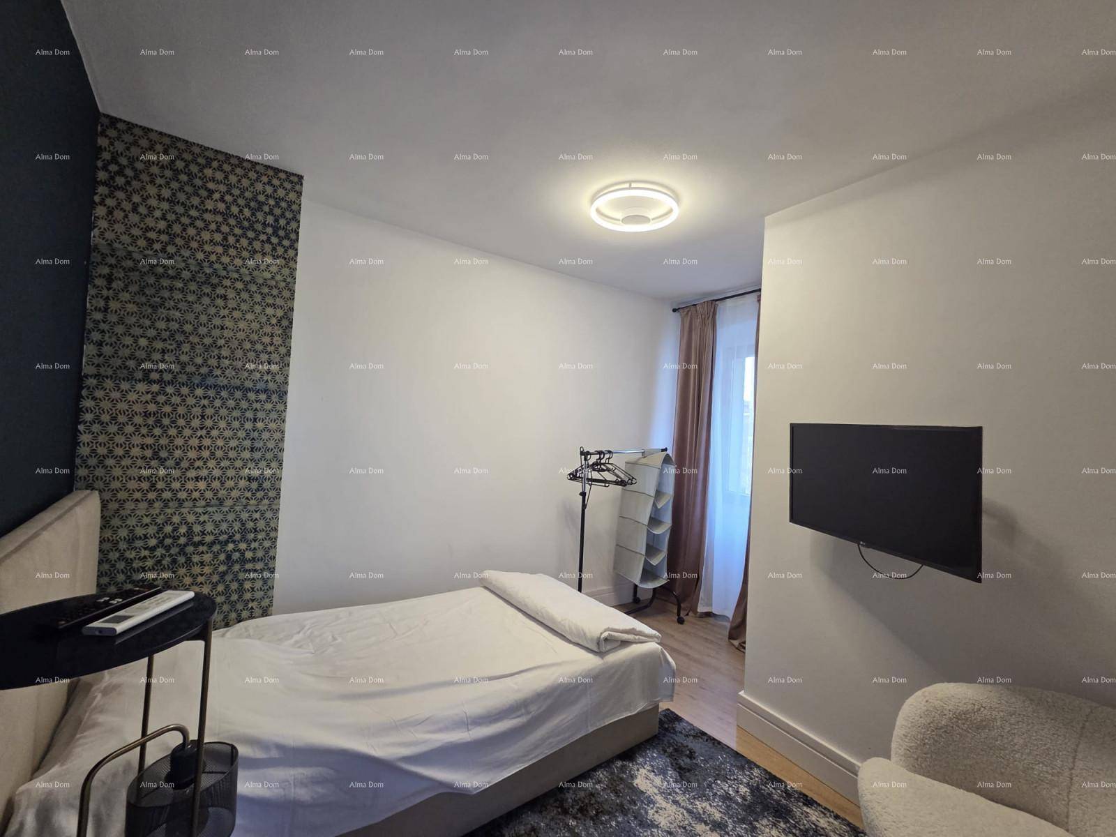 Schlafzimmer mit Bett, Wandfernseher und einem Teppich, ergänzt durch eine Kleiderstange.