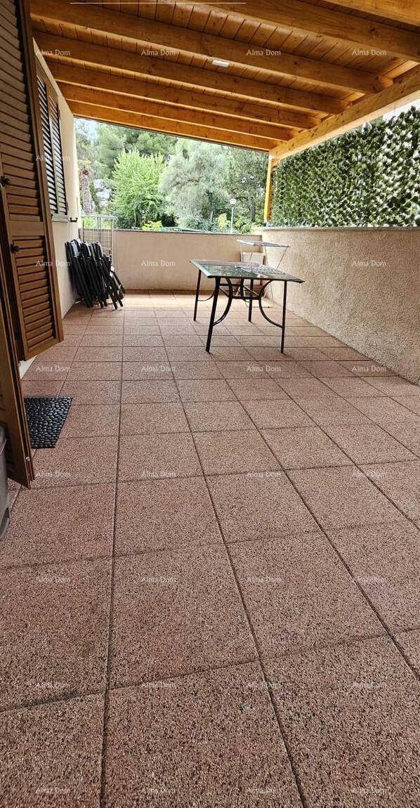 Überdachte Terrasse mit Fliesenboden und einem kleinen Tisch, umgeben von Grün.