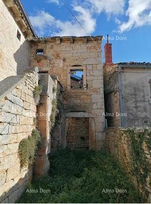 Altes, verfallenes Steinhaus mit sichtbaren Mauerresten und überwuchertem Gelände unter blauem Himmel.