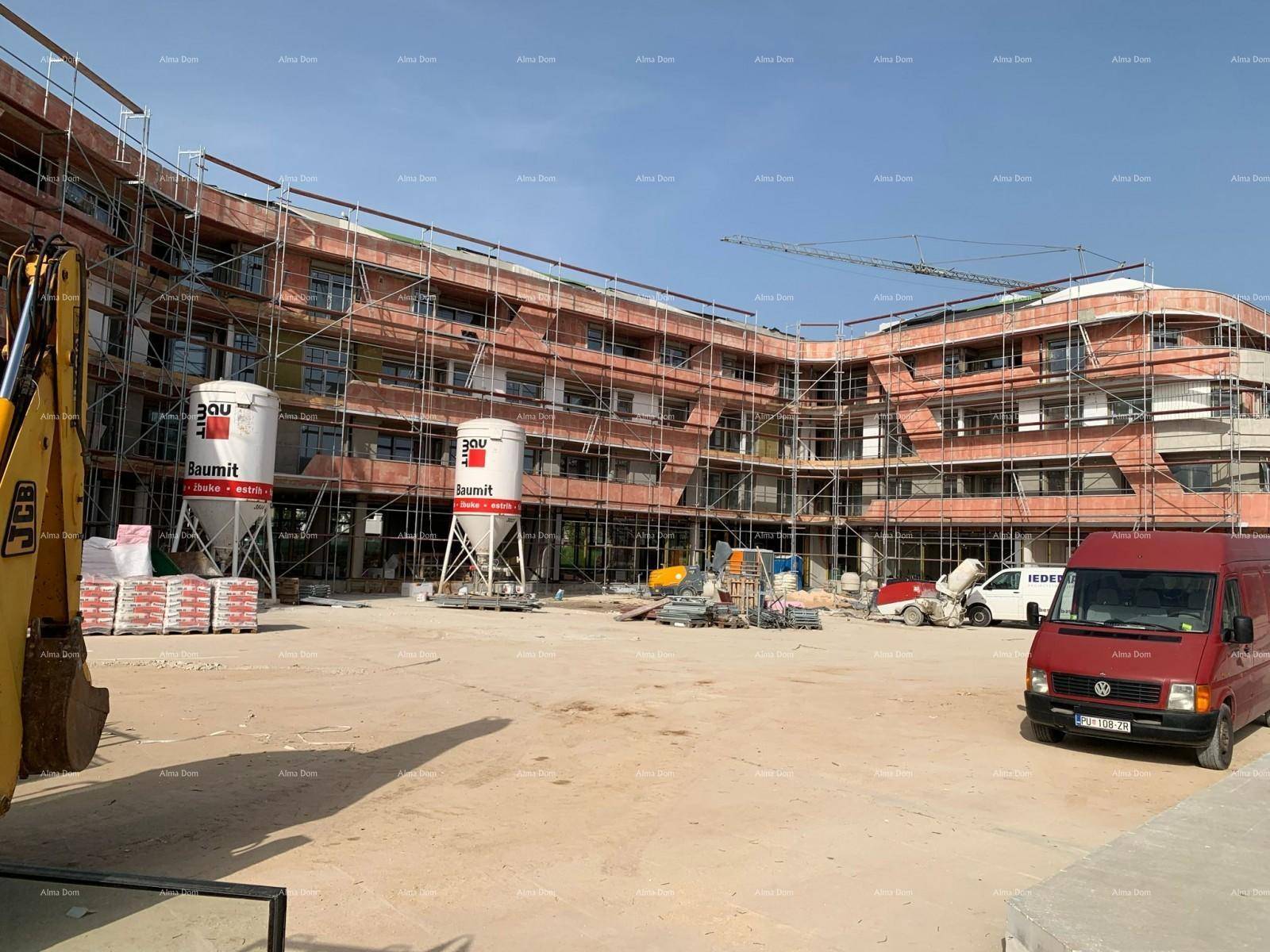 Baustelle der Wohnanlage mit Gerüst, Baumaterialien und Baufahrzeugen vor der Fassade.