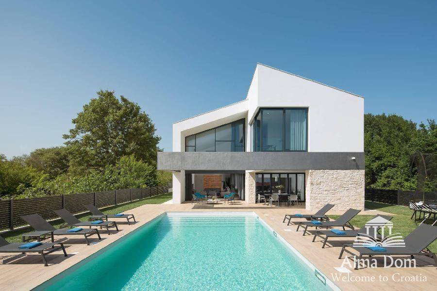 Elegante moderne Villa mit großem Swimmingpool, umgeben von Grünflächen und Sonnenliegen.