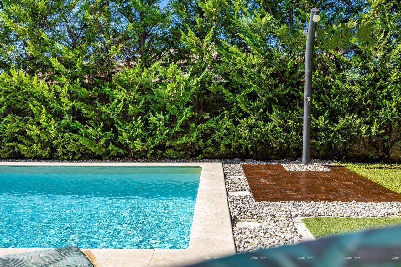 Detailansicht des Poolbereichs mit Außendusche, Kies und Kunstrasen, umgeben von einer Hecke.