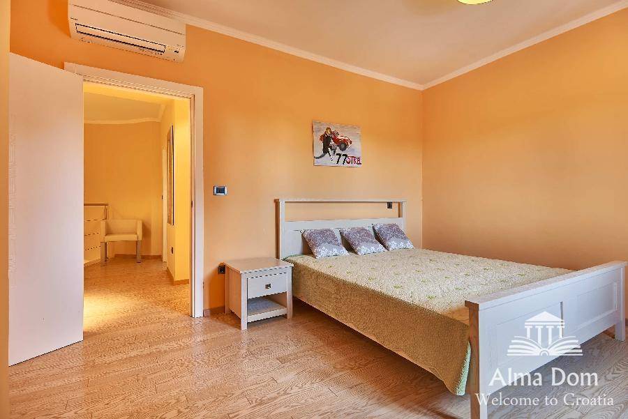 Helles Schlafzimmer mit orangefarbenen Wänden, Holzboden und Klimaanlage.