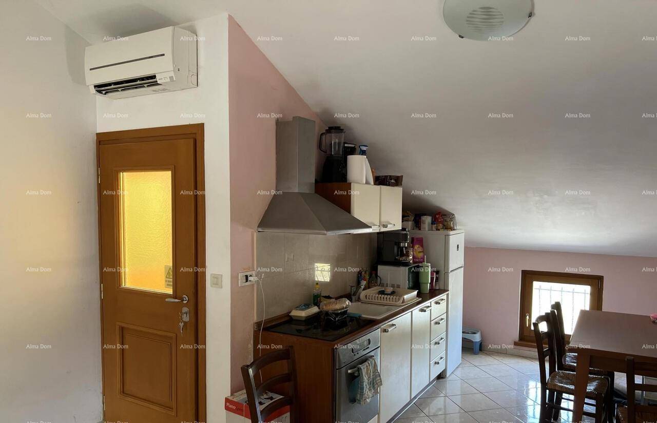Kleine Küche im Dachgeschoss mit Einbauschränken, Essbereich und Klimaanlage unter schräger Decke.