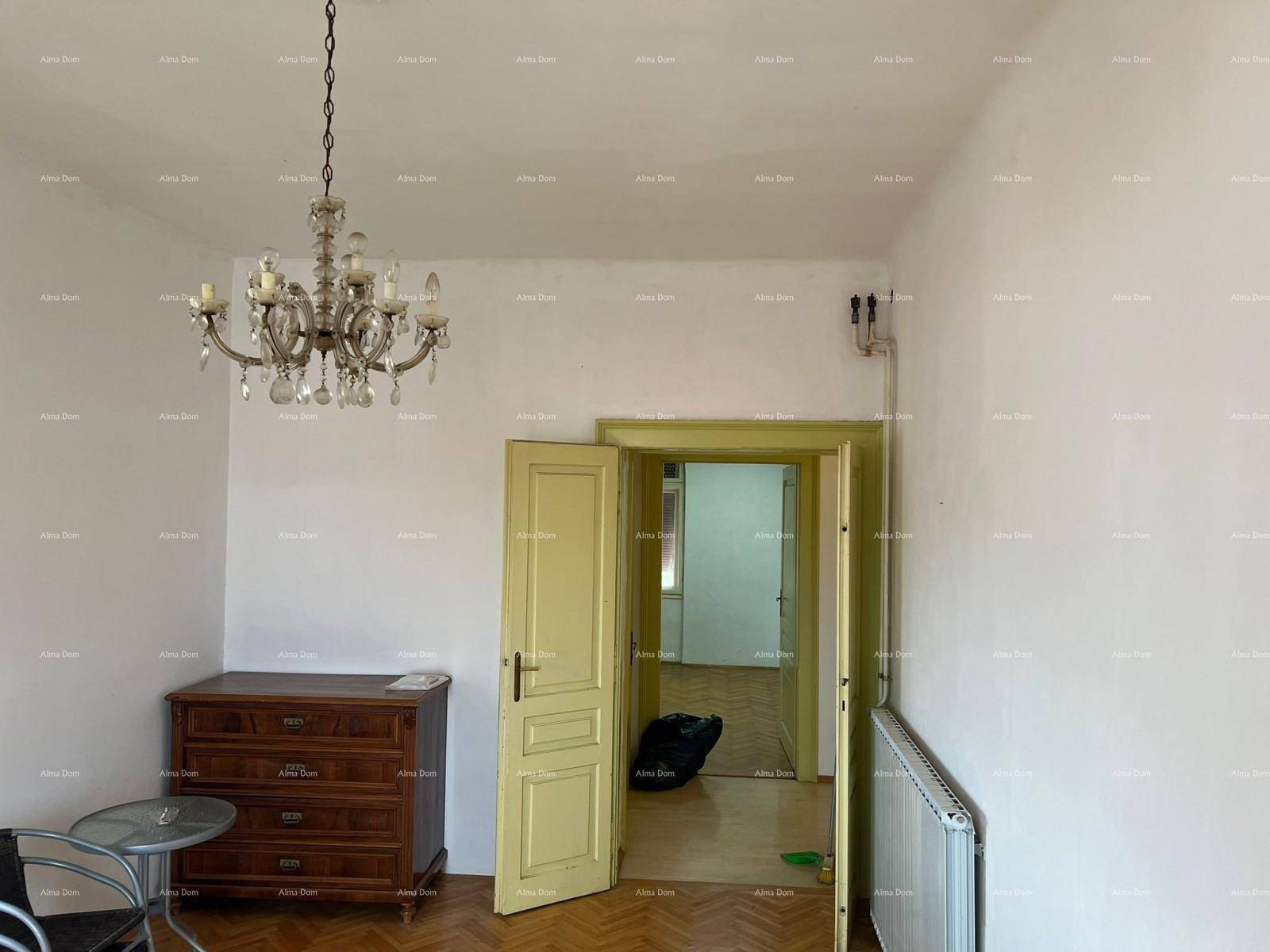 Wohnzimmer mit Fischgrätparkett, einem antiken Holzschrank und einem Kronleuchter, der den Raum erhellt.