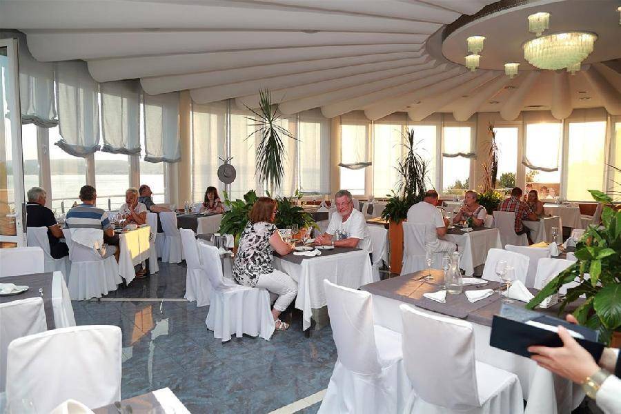 Heller Speisesaal mit großen Fenstern, die einen Panoramablick auf das Meer bieten, und vielen Gästen.