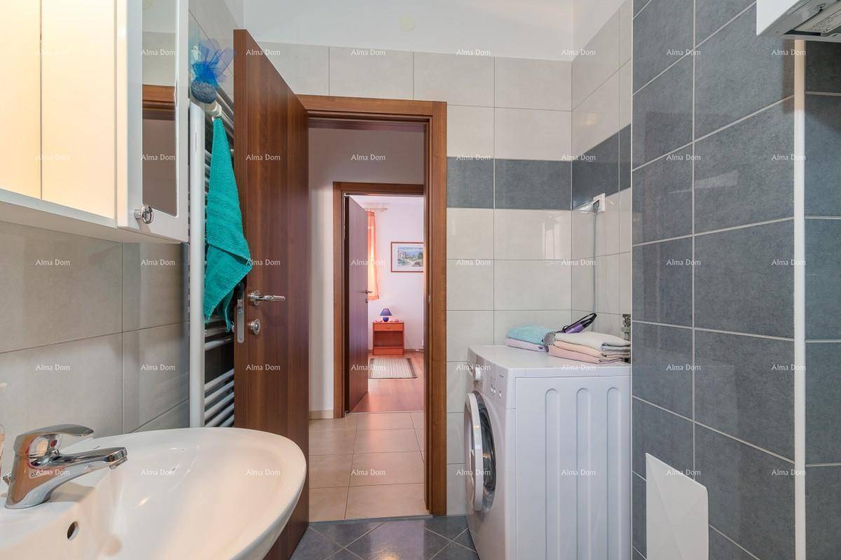 Badezimmer mit Waschmaschine und Zugang zu einem weiteren Raum, gefliest in Grau und Weiß.