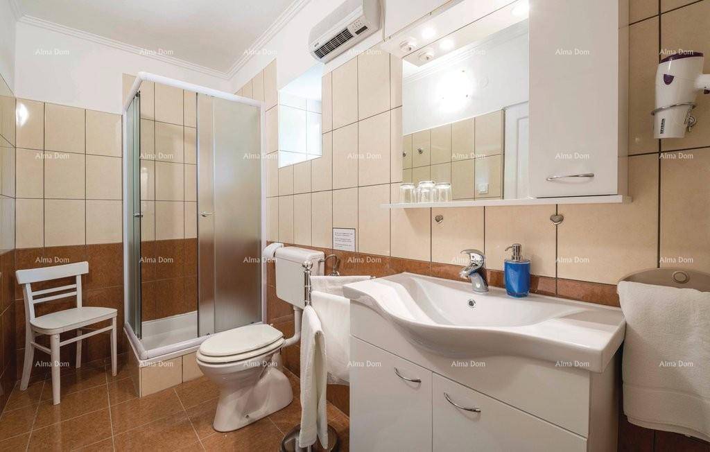 Funktionales Badezimmer mit Duschkabine, WC, Waschbecken und Klimaanlage, ausgestattet mit beigefarbenen Fliesen.