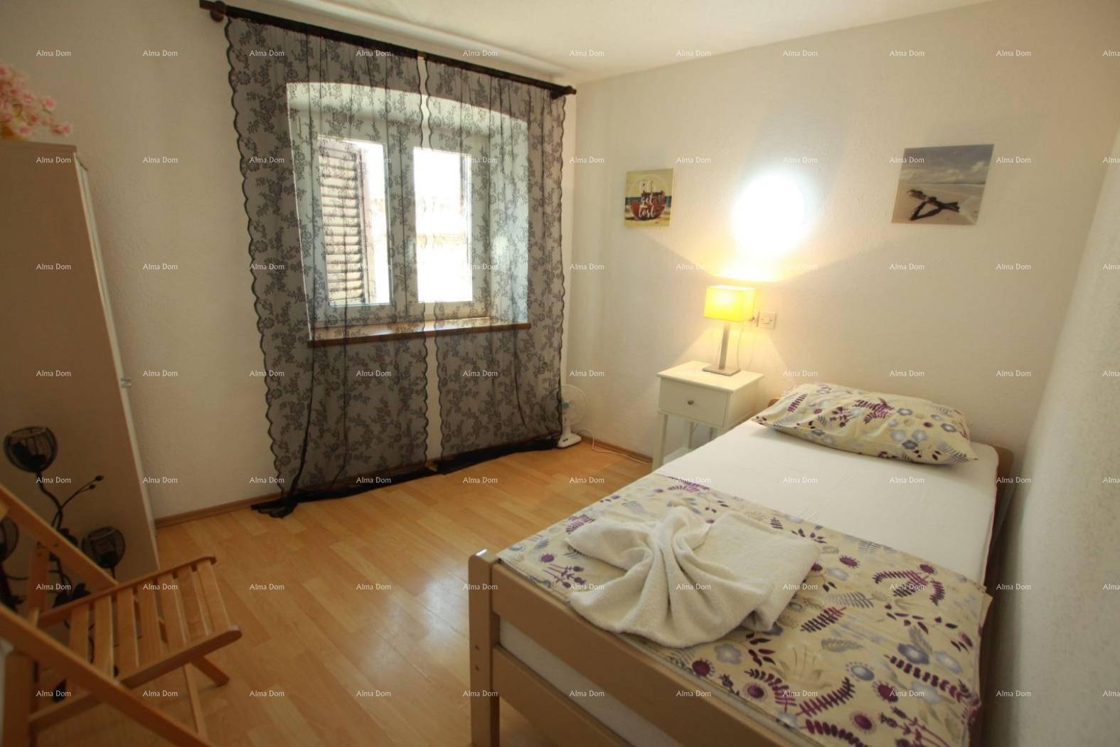 Helles Schlafzimmer mit Einzelbett, Holzfußboden und Fenster mit dunklen Vorhängen.