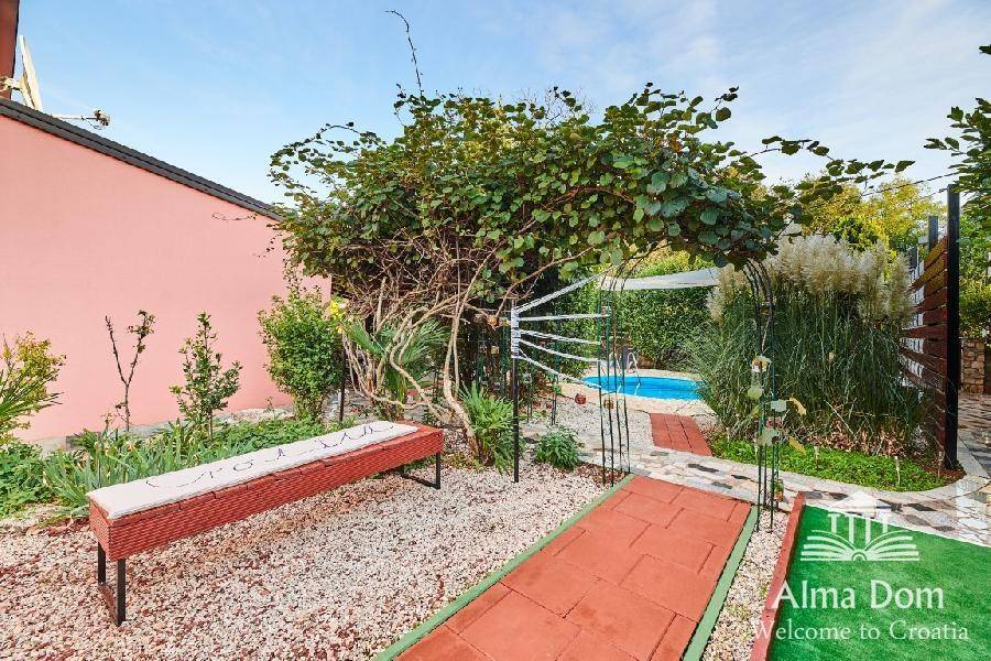 Gartenweg mit einer Bank, der zum Poolbereich führt, umgeben von vielfältiger Bepflanzung.