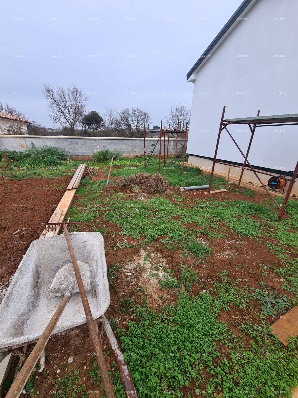 Gartenbereich im Bau mit Erdboden, einigen Pflanzen und Baustellengeräten im Hintergrund.