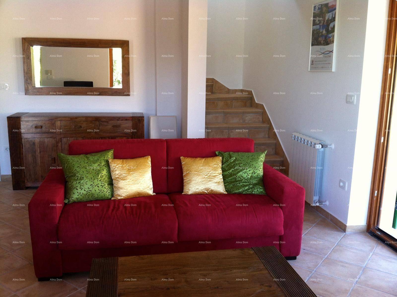Gemütliches Wohnzimmer mit rotem Sofa, Holztisch und Treppe zum Obergeschoss, auf Fliesenboden.