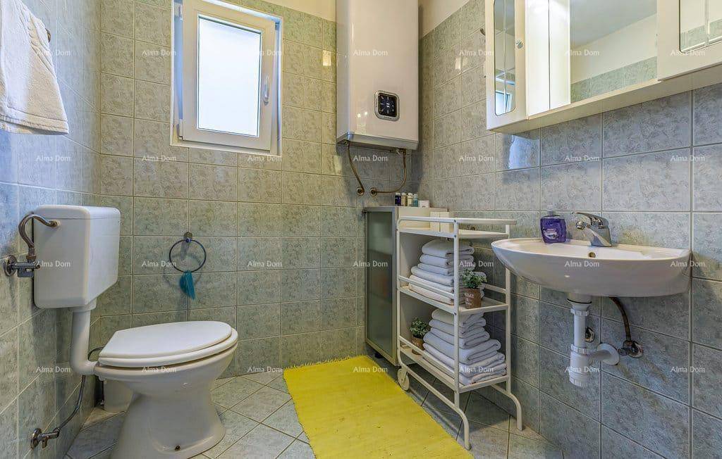 Badezimmer mit hellblauen Fliesen, Toilette, Waschbecken und Fenster für Belüftung.