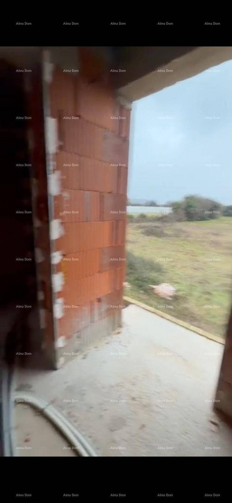 Blick aus einer großen Fensteröffnung im Rohbau auf die umliegende grüne Landschaft.