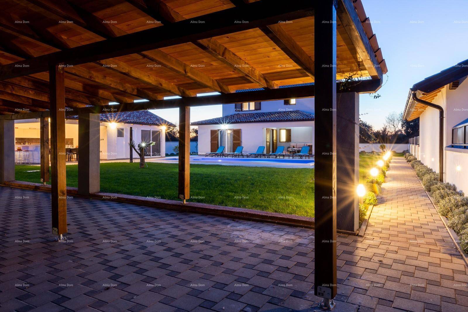 Holzpergola über einem gepflasterten Bereich mit beleuchtetem Weg und Blick auf das Haus und den Pool.