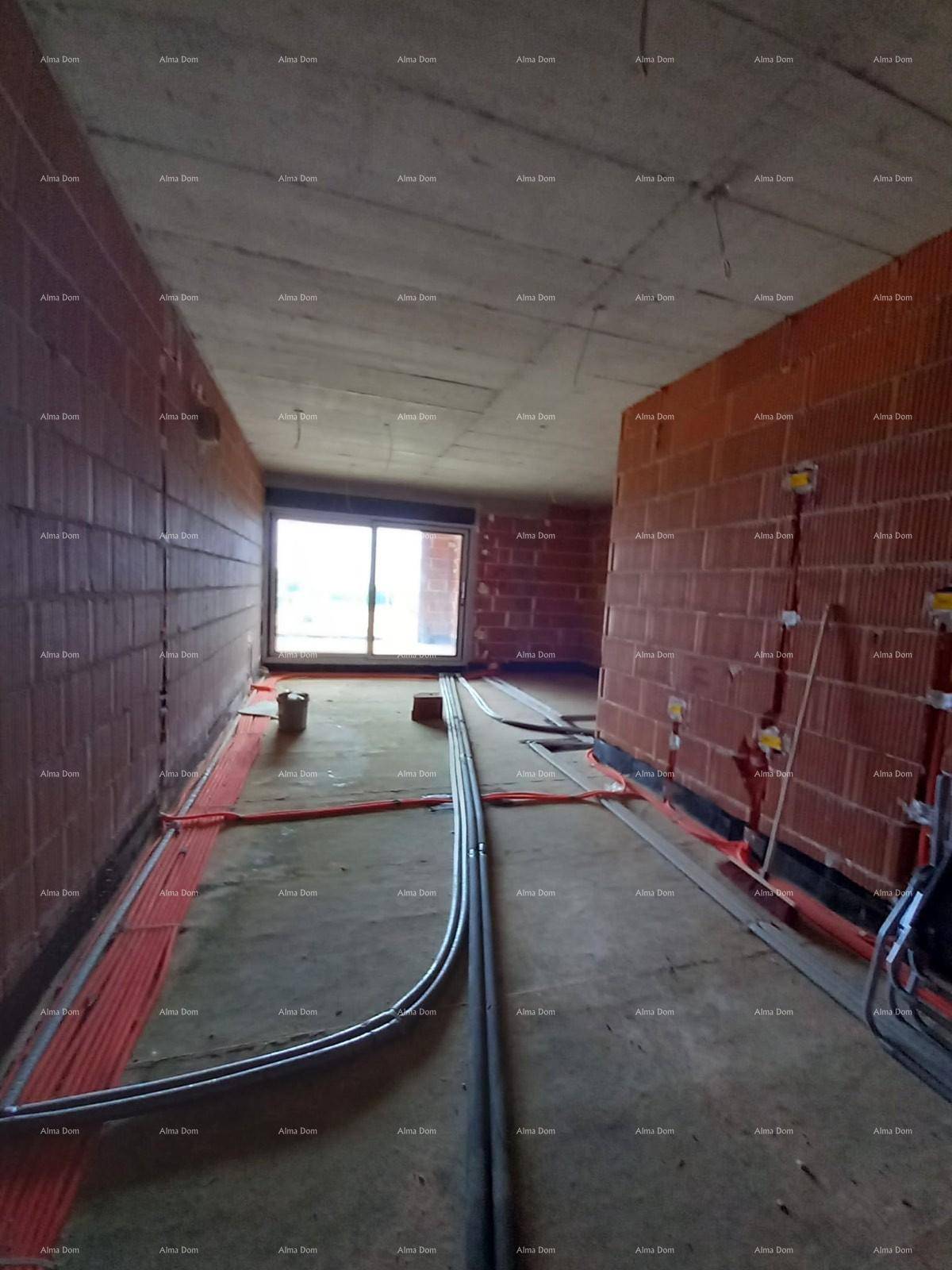 Langer Raum im Rohbau mit großem Fenster am Ende und verlegten Installationsrohren.