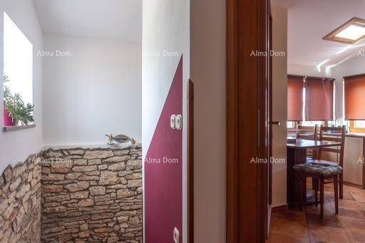 Flur mit Steinwand und Holztür, führt in einen hellen Essbereich mit Fenster.