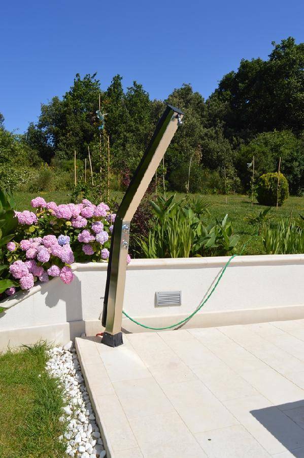 Außendusche auf einer gefliesten Fläche, umgeben von blühenden Hortensien und grüner Vegetation.