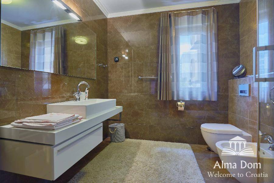 Luxuriöses Badezimmer mit braunen Marmorfliesen, modernem Waschtisch, Bidet und Fenster.