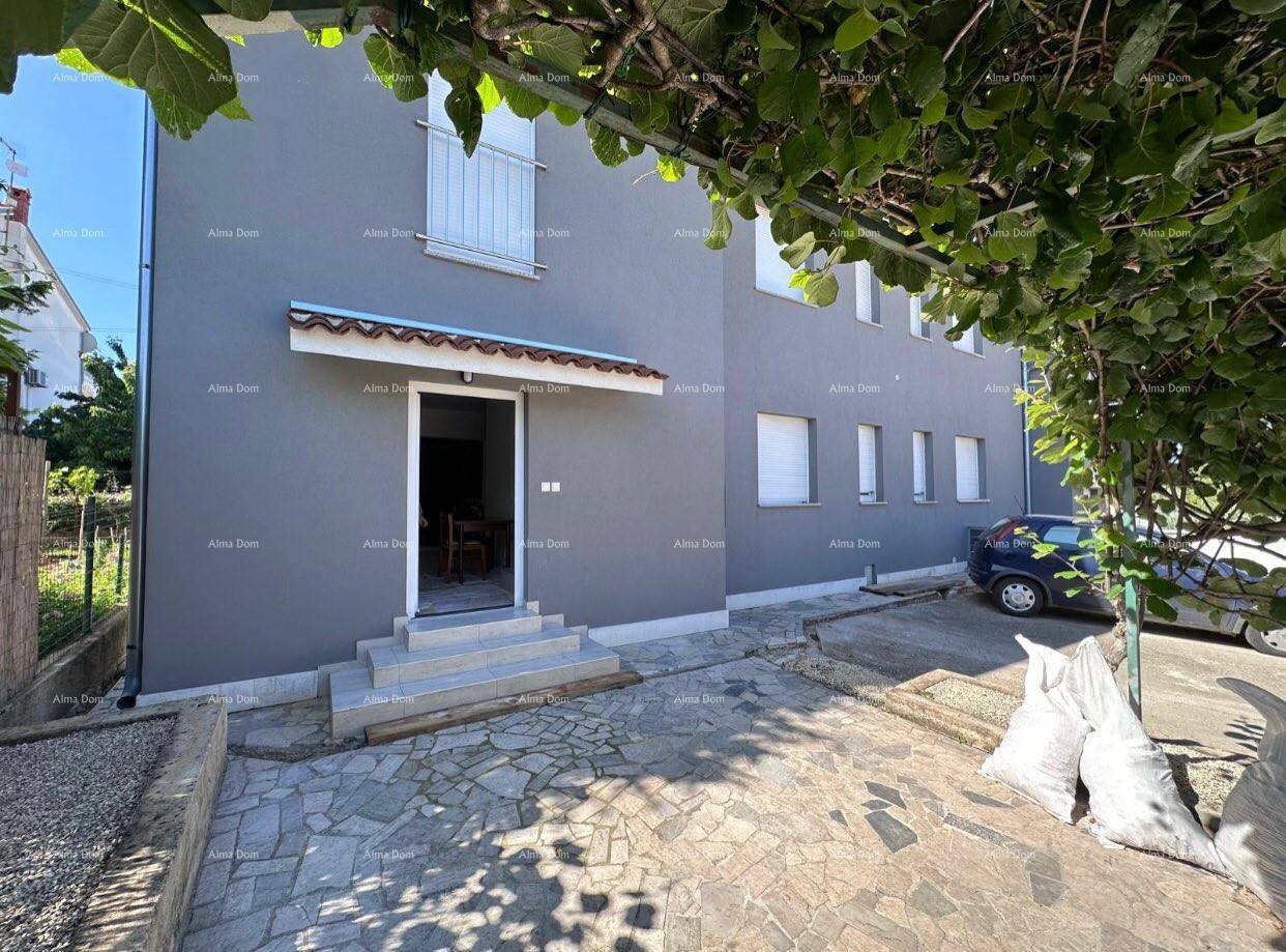 Nahaufnahme des Hauseingangs mit grauer Fassade, Steinfliesen und einem überdachten Bereich.