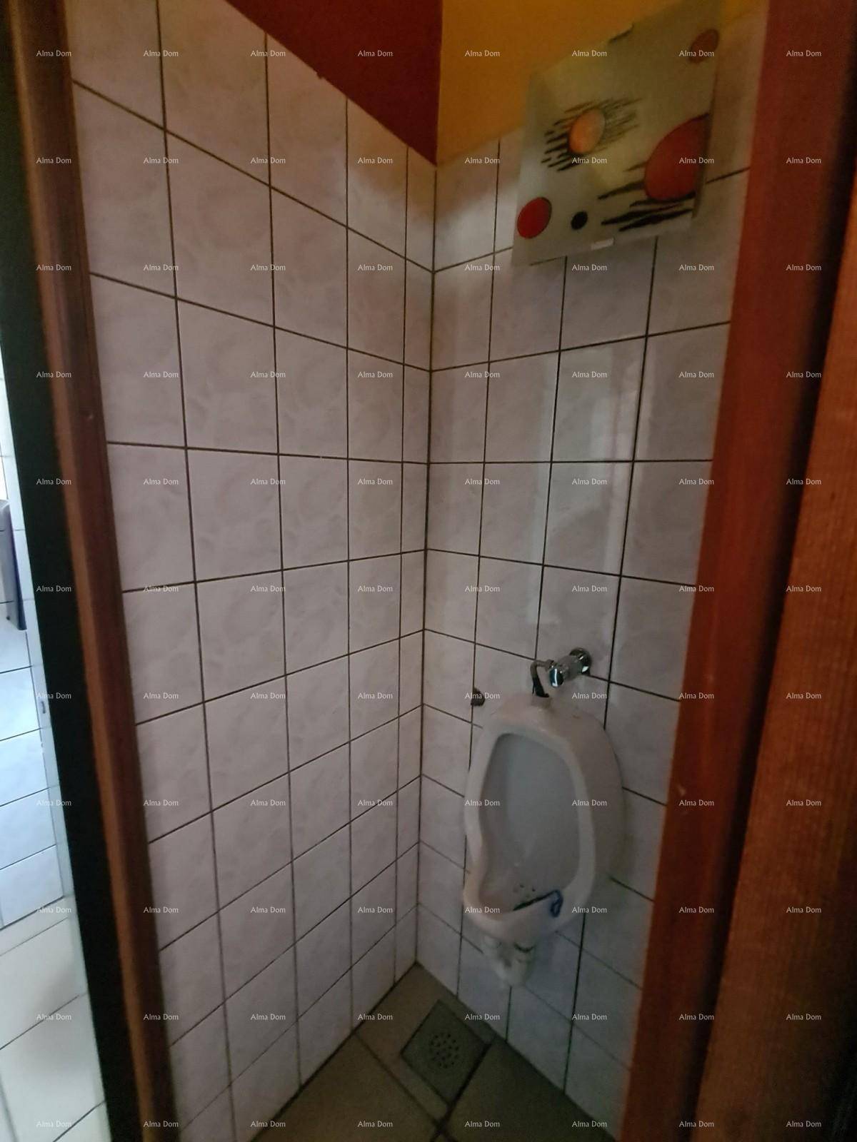 Herrentoilette mit weißen Fliesen, einem Urinal und einem Spender an der Wand.