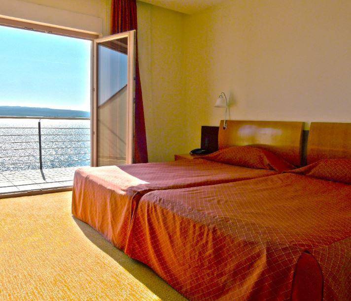 Helles Schlafzimmer mit zwei Einzelbetten, Teppichboden und direktem Zugang zu einem Balkon mit Meerblick.