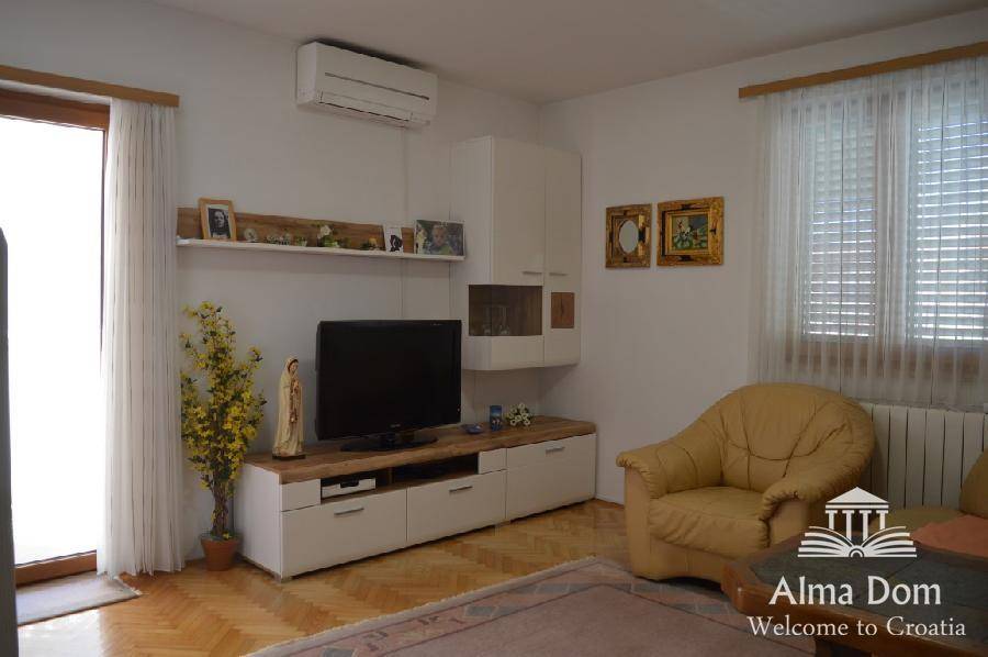 Wohnzimmer mit Fernseher, Klimaanlage und Zugang zum Balkon, hell und freundlich gestaltet.