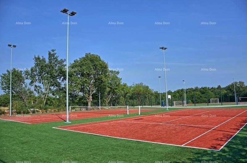 Zwei Tennisplätze mit rotem Belag und Flutlicht inmitten grüner Natur.