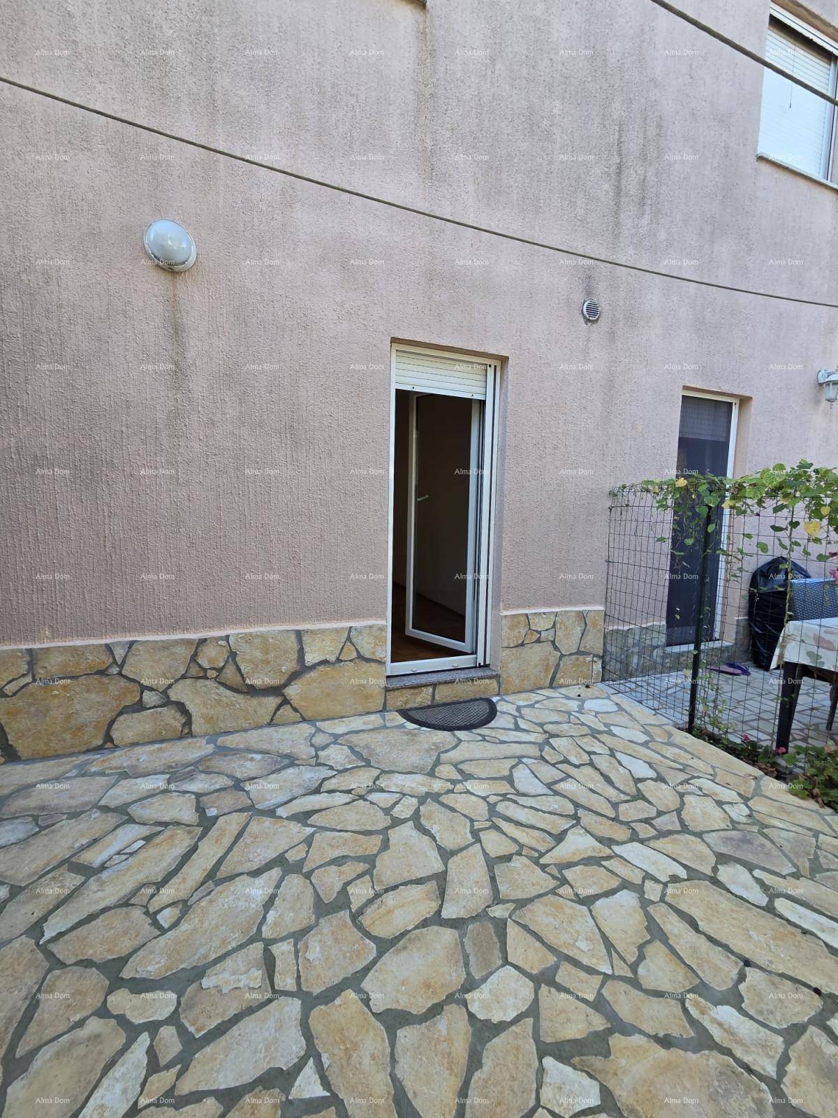 Außenansicht des Gebäudes mit Zugang zu einem gepflasterten Terrassenbereich und Rollläden.