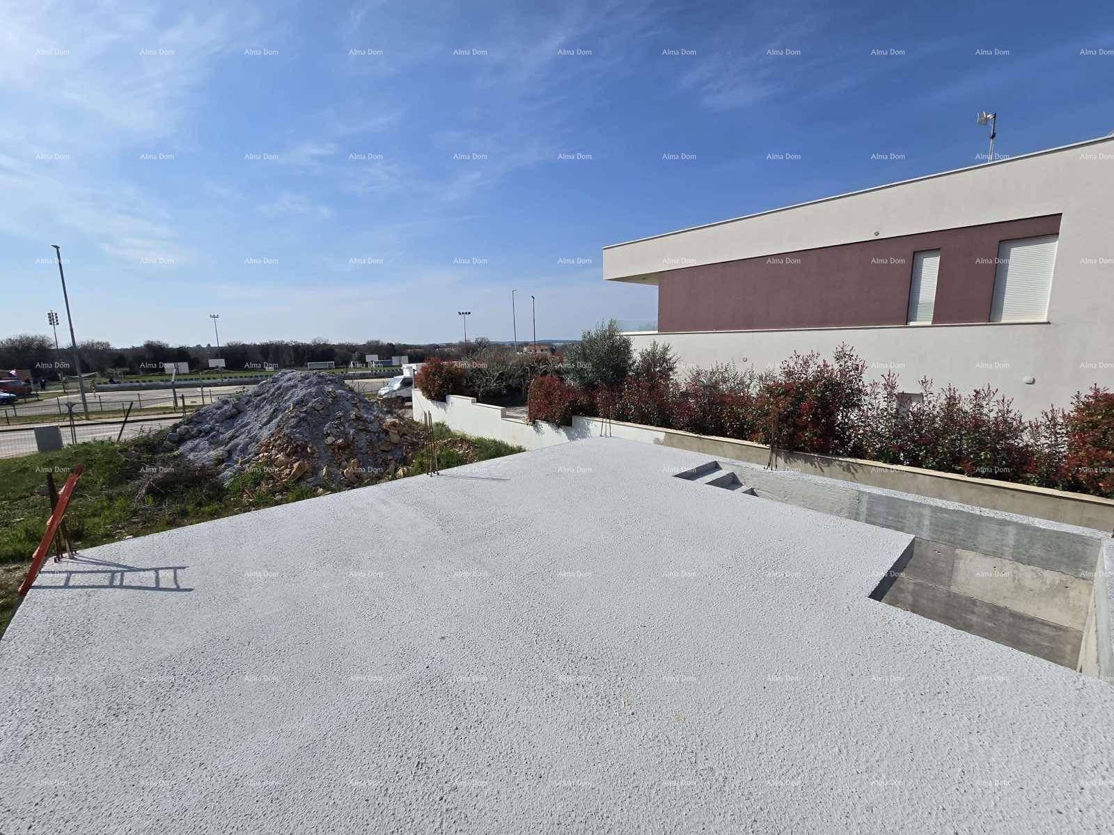 Betonierte Bodenplatte einer Baustelle mit Blick auf ein modernes Gebäude und eine Schotterhalde.