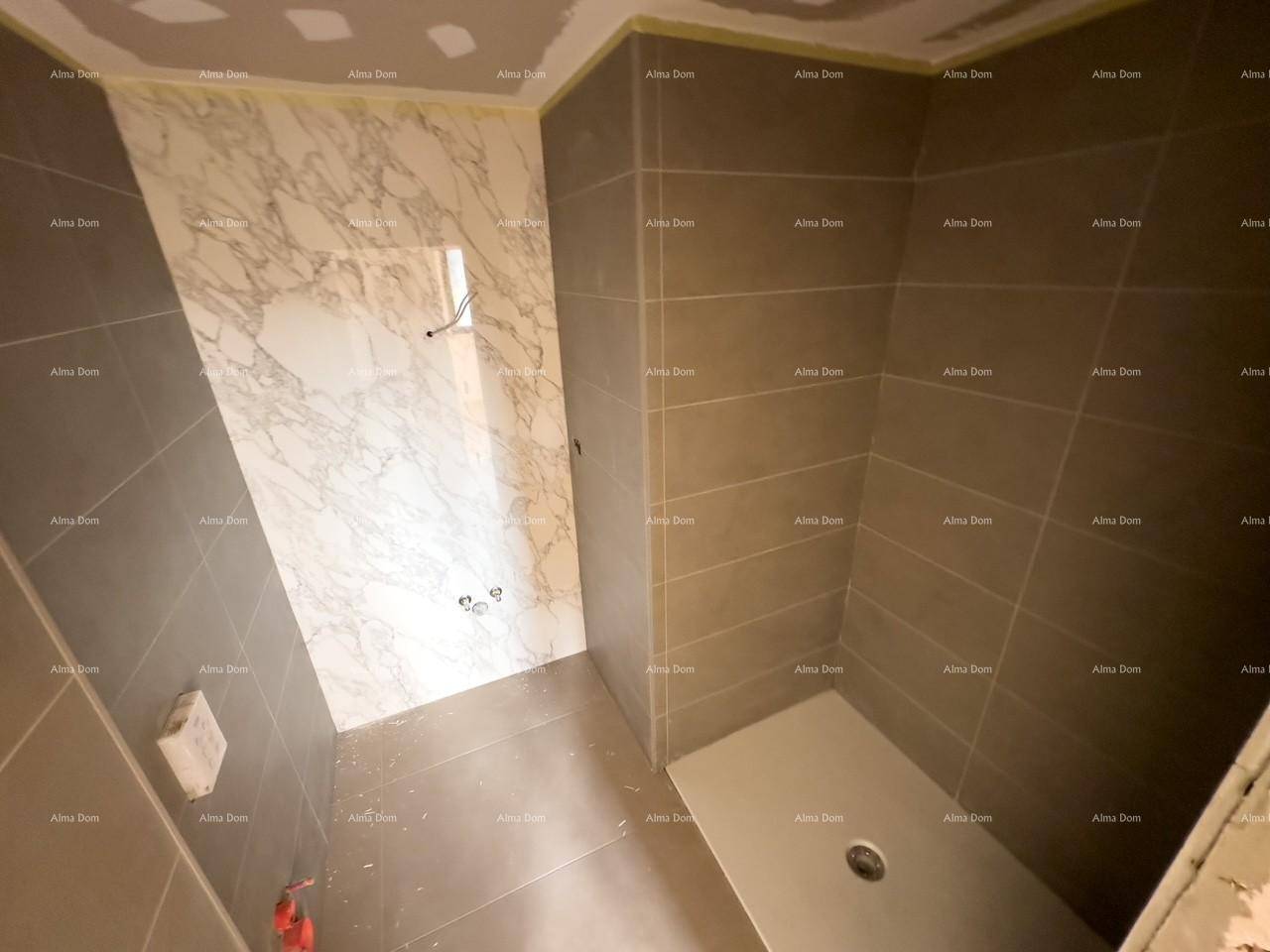 Badezimmer im Rohbau mit grauen Fliesen und einer vorbereiteten Duschzone.