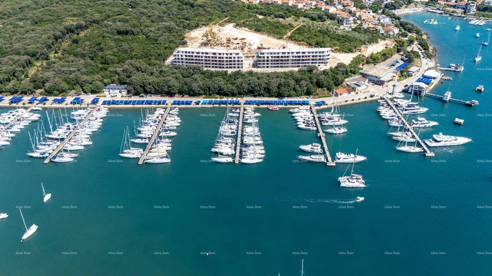 Panoramablick auf einen belebten Yachthafen und neue Wohngebäude in Küstennähe unter strahlend blauem Himmel.