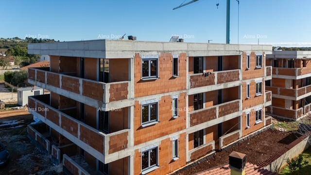 Gebäude im Rohbau mit installierten Fenstern und Balkonen, umgeben von ländlicher Landschaft.