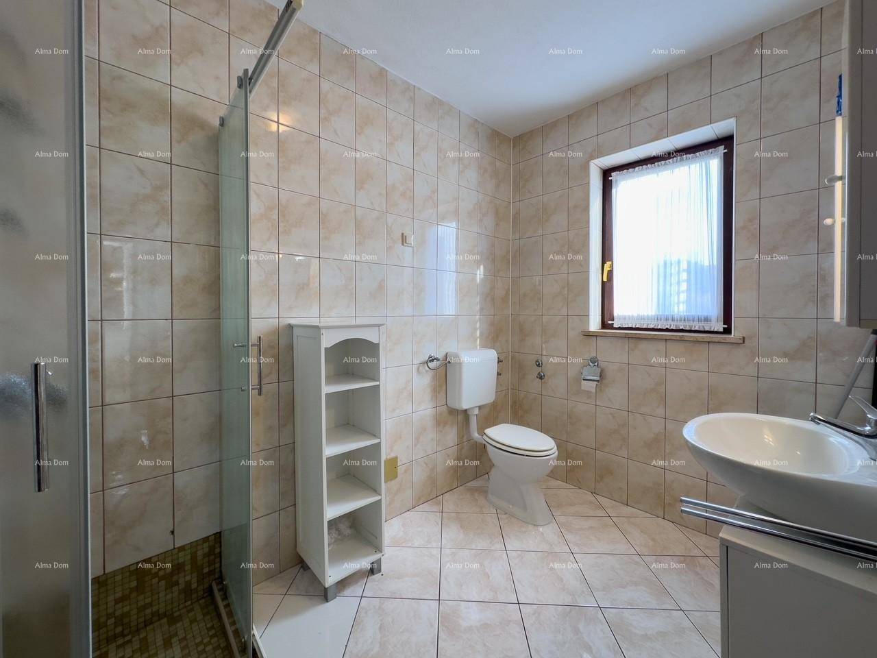 Helles Badezimmer mit beigefarbenen Fliesen, Duschkabine, Toilette und Fenster.