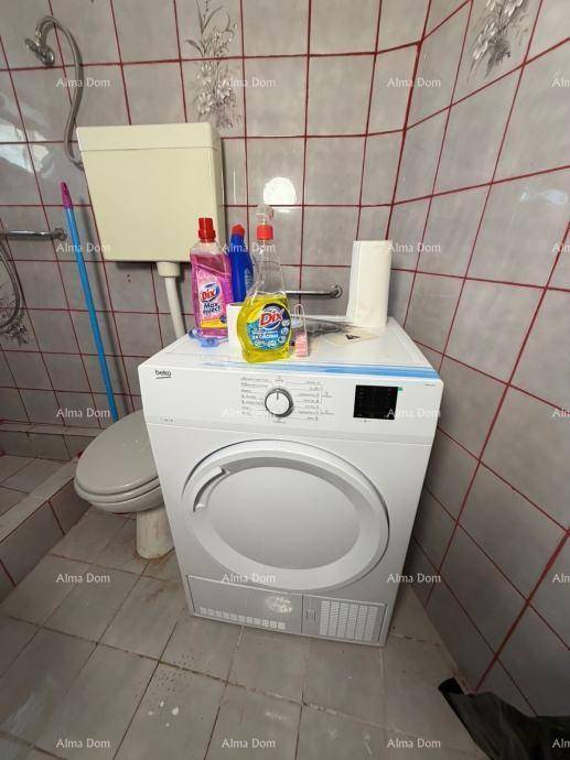Gefliestes Badezimmer mit Toilette und einer Waschmaschine, die auch als Trockner dient.