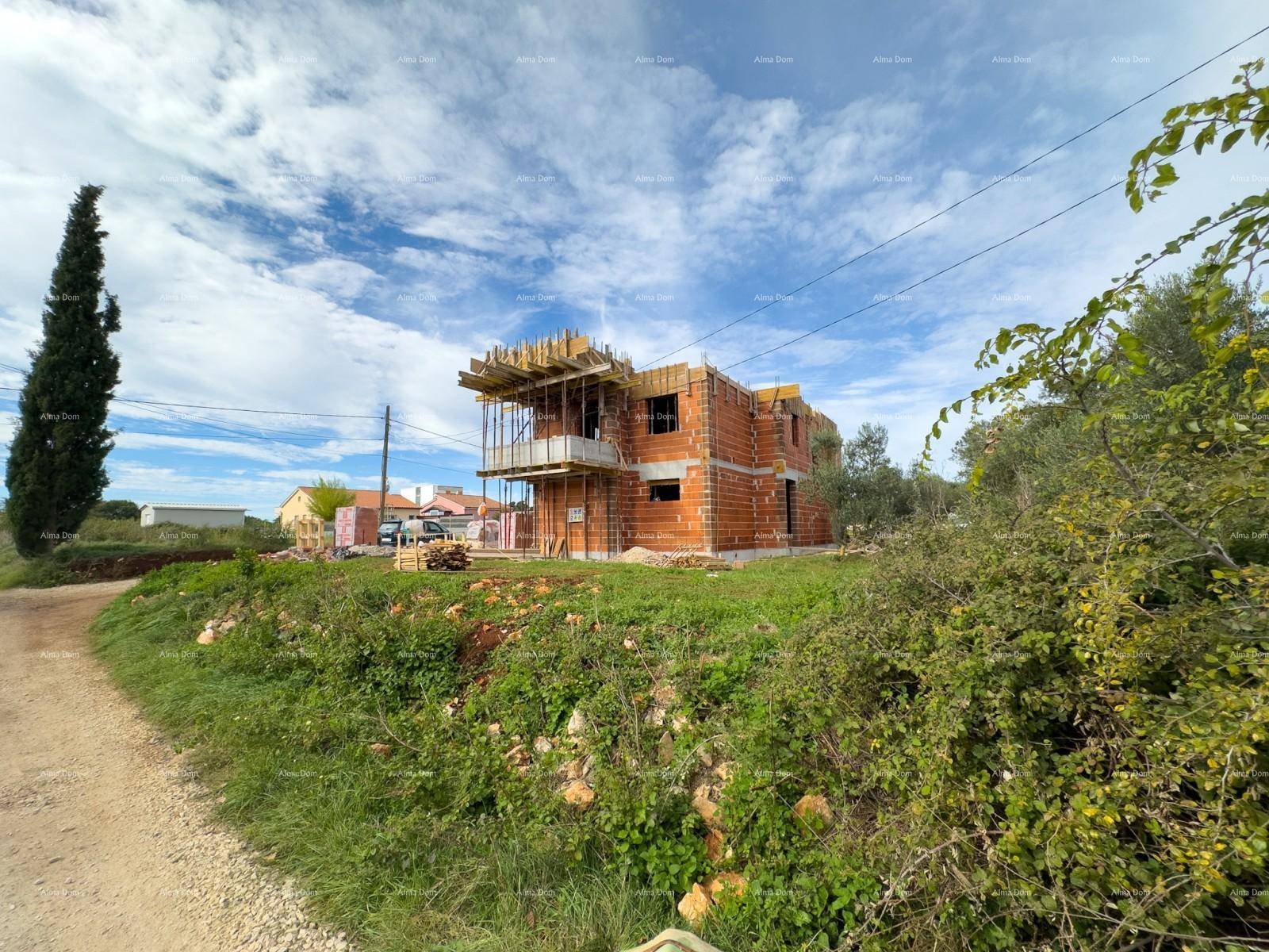 Neubau im Rohbauzustand, umgeben von grüner Vegetation und einem Feldweg unter blauem Himmel.