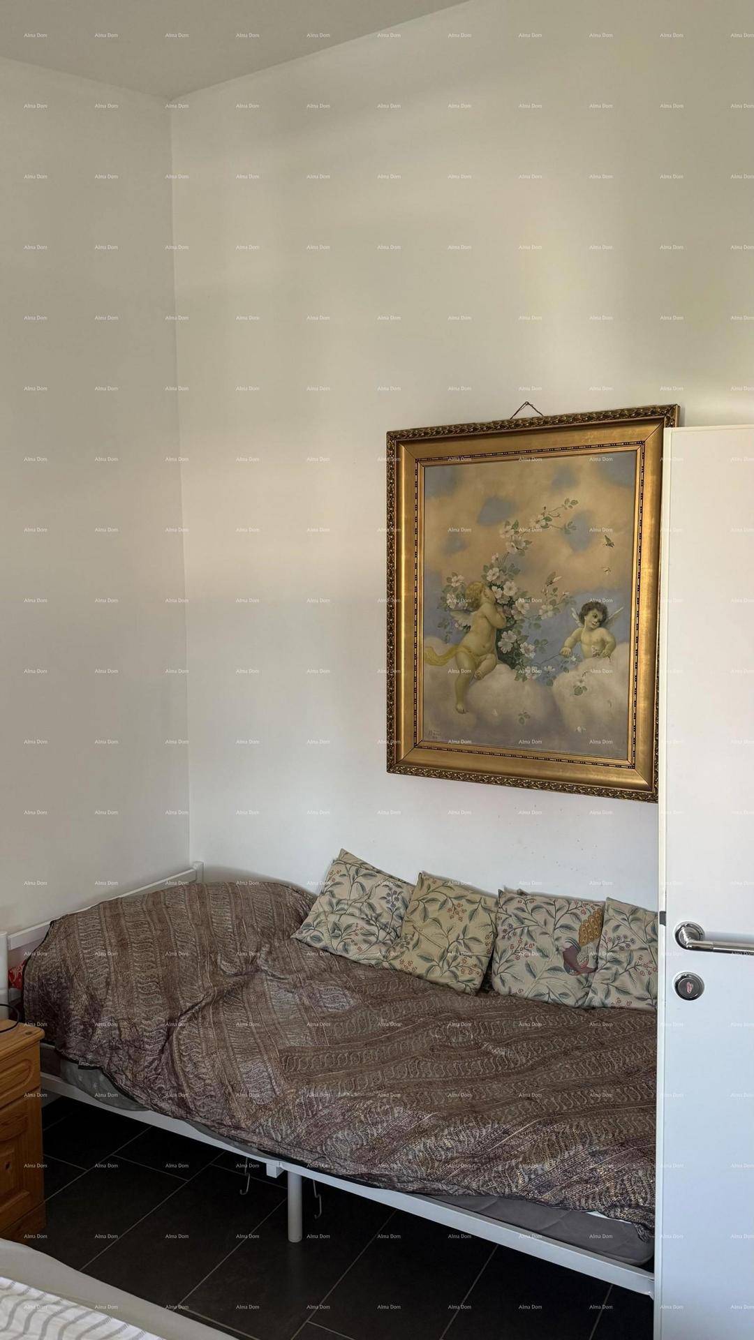 Kleines Schlafzimmer mit Einzelbett und einem gerahmten Bild an der Wand, auf dunklen Fliesen.