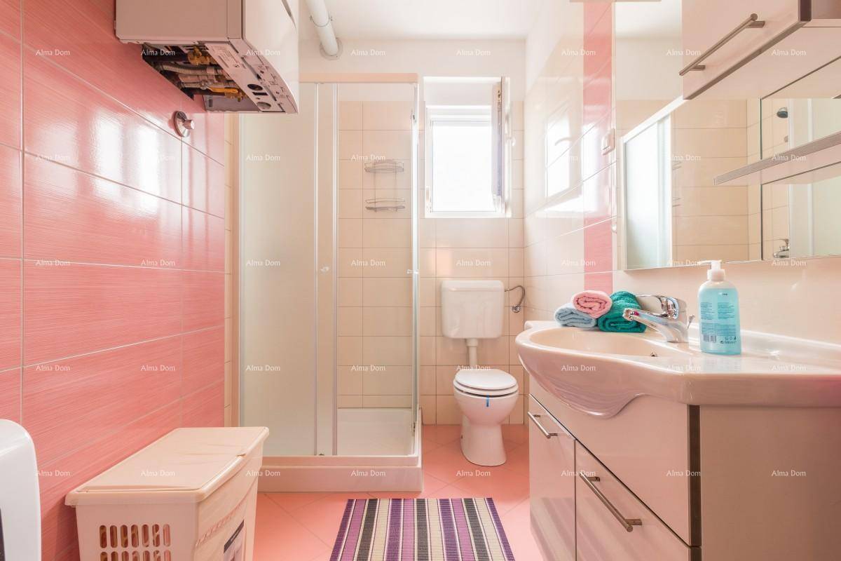 Badezimmer mit rosa Fliesen, Duschkabine, Waschbecken und Toilette, ausgestattet mit einem Fenster.