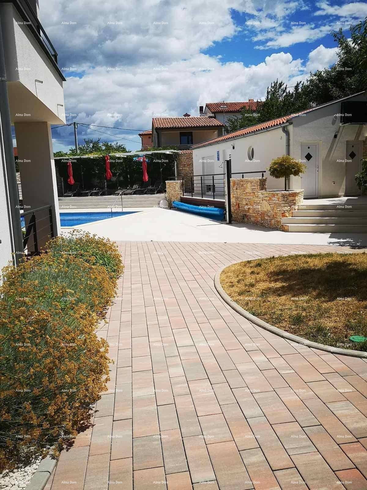 Gepflasterter Weg führt durch den Gartenbereich mit mediterranen Pflanzen und Blick auf die Gebäude.