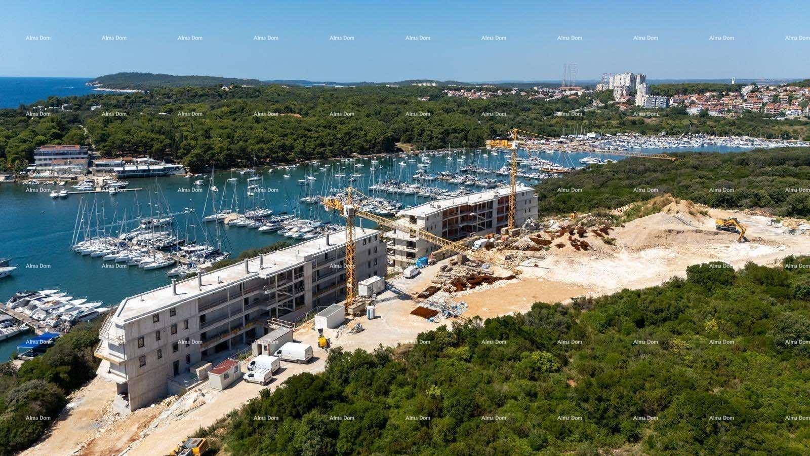 Luftaufnahme einer großen Baustelle neben einem Yachthafen mit im Bau befindlichen Gebäuden und Kränen.
