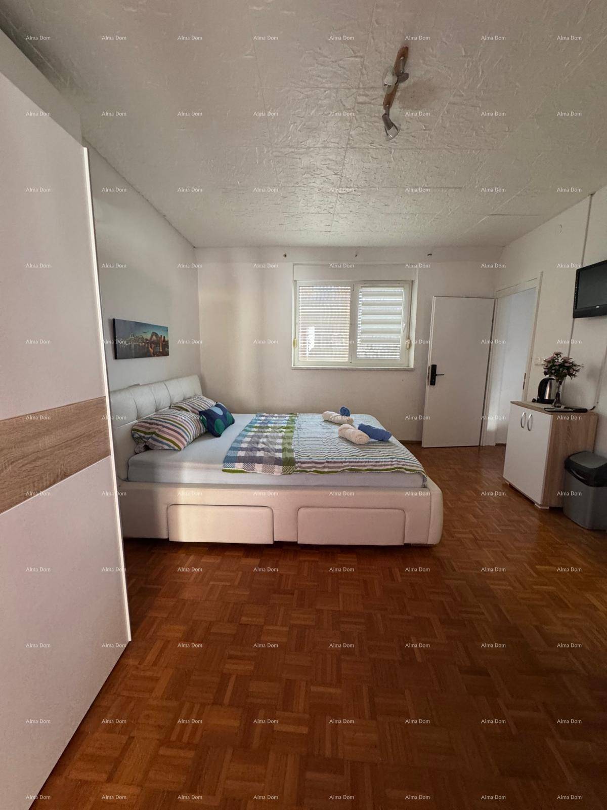 Schlafzimmer mit Doppelbett und Parkettboden, Fenster mit Jalousien und kleiner Kommode.