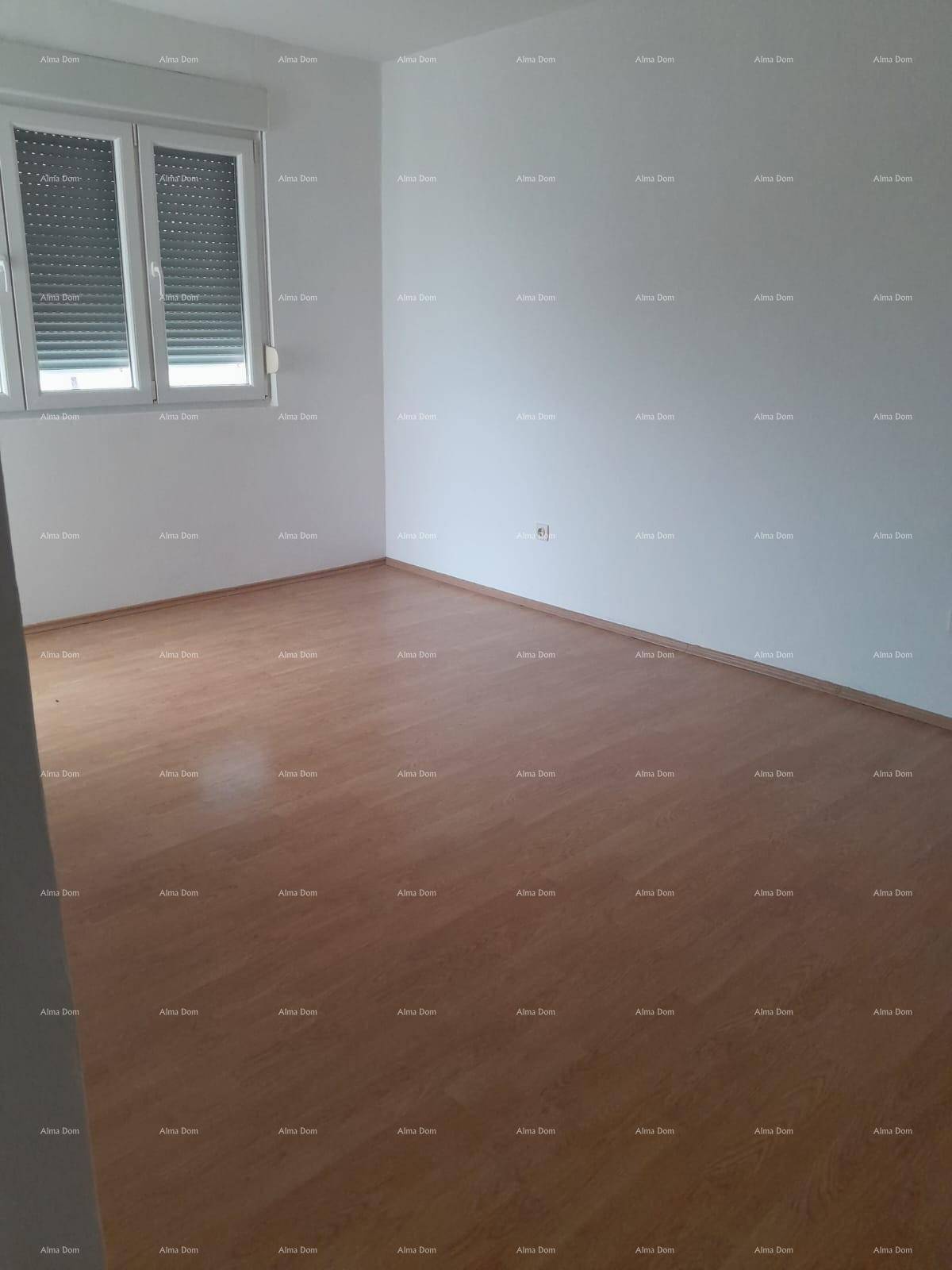 Leeres Zimmer mit hellem Laminatboden und einem Fenster mit geschlossenen Rollläden.